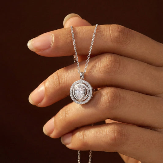 Hand holding a silver necklace with a diamond pendant against a dark background