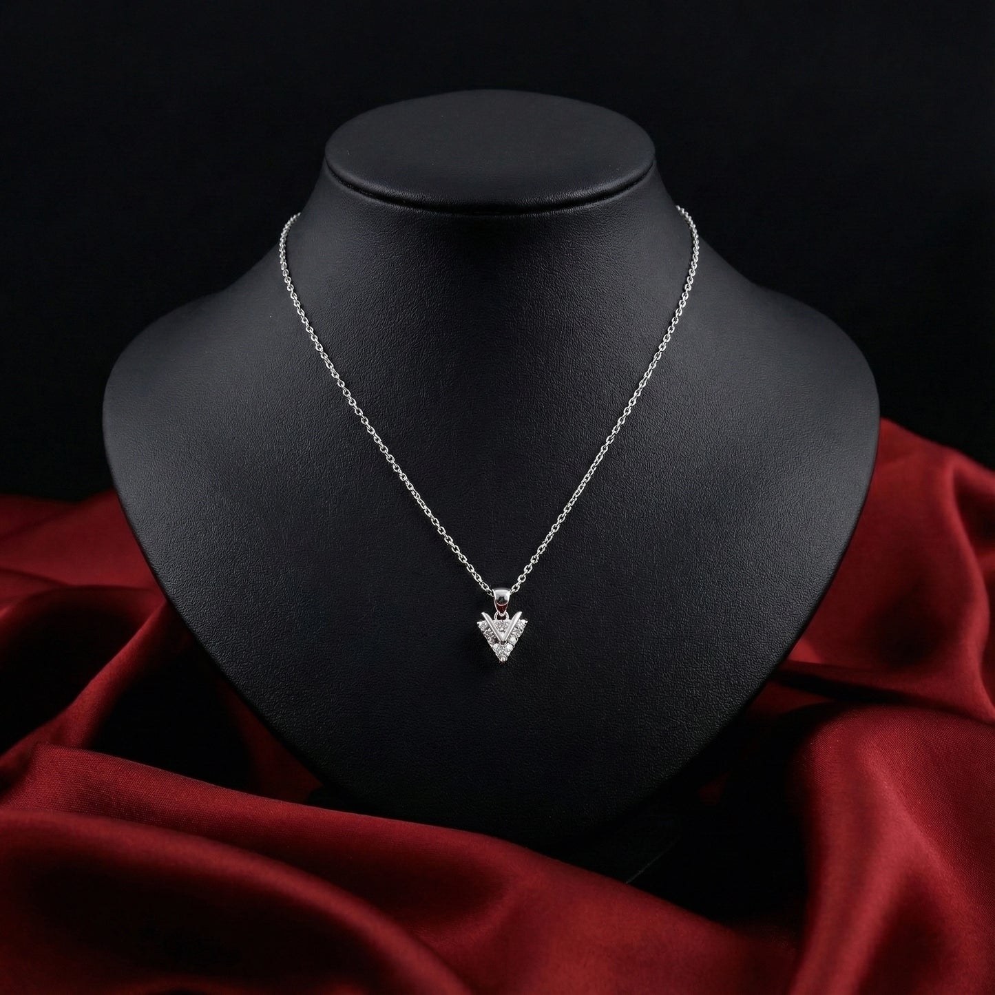 Silver necklace with a heart-shaped pendant on a black mannequin bust against a red fabric background