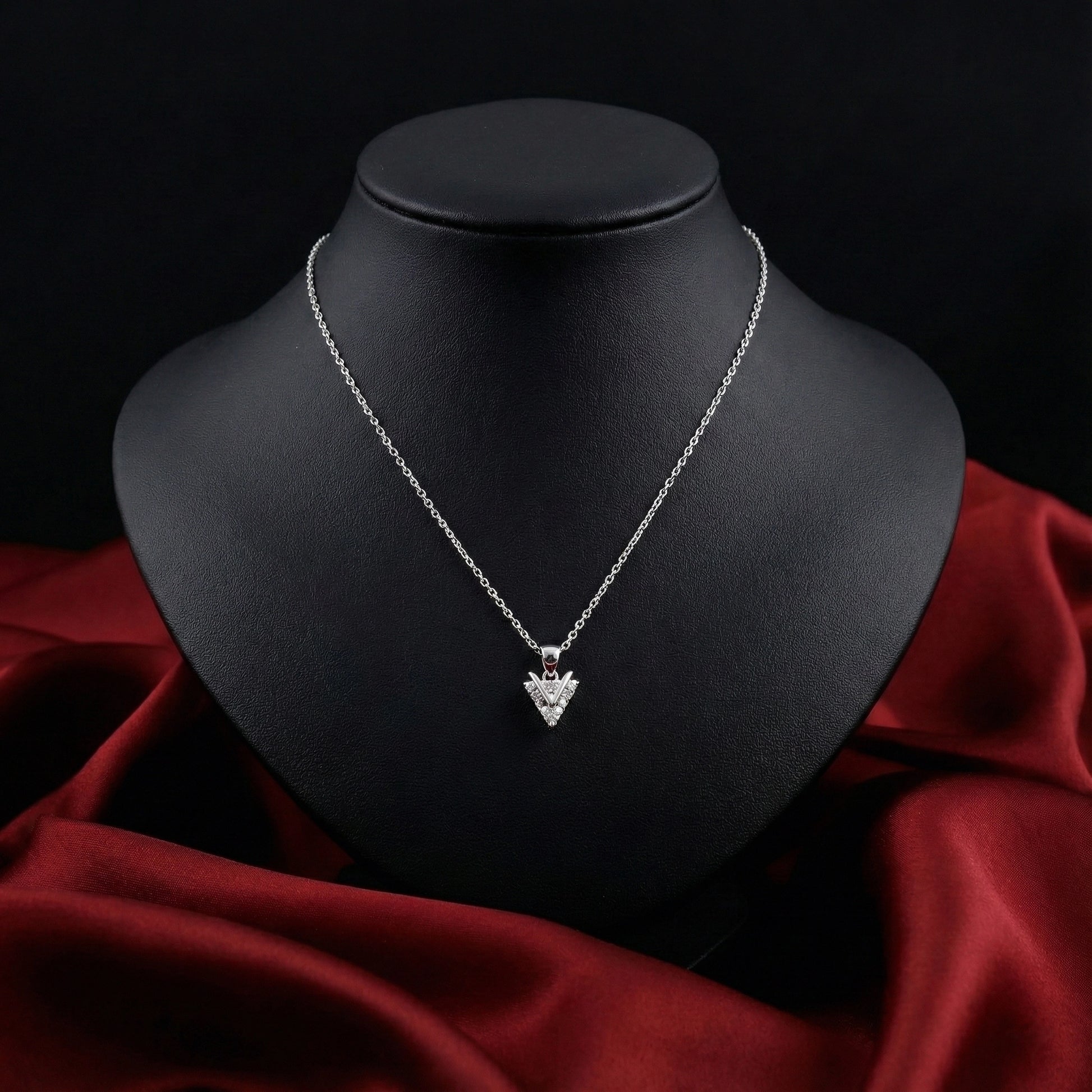 Silver necklace with a heart-shaped pendant on a black mannequin bust against a red fabric background