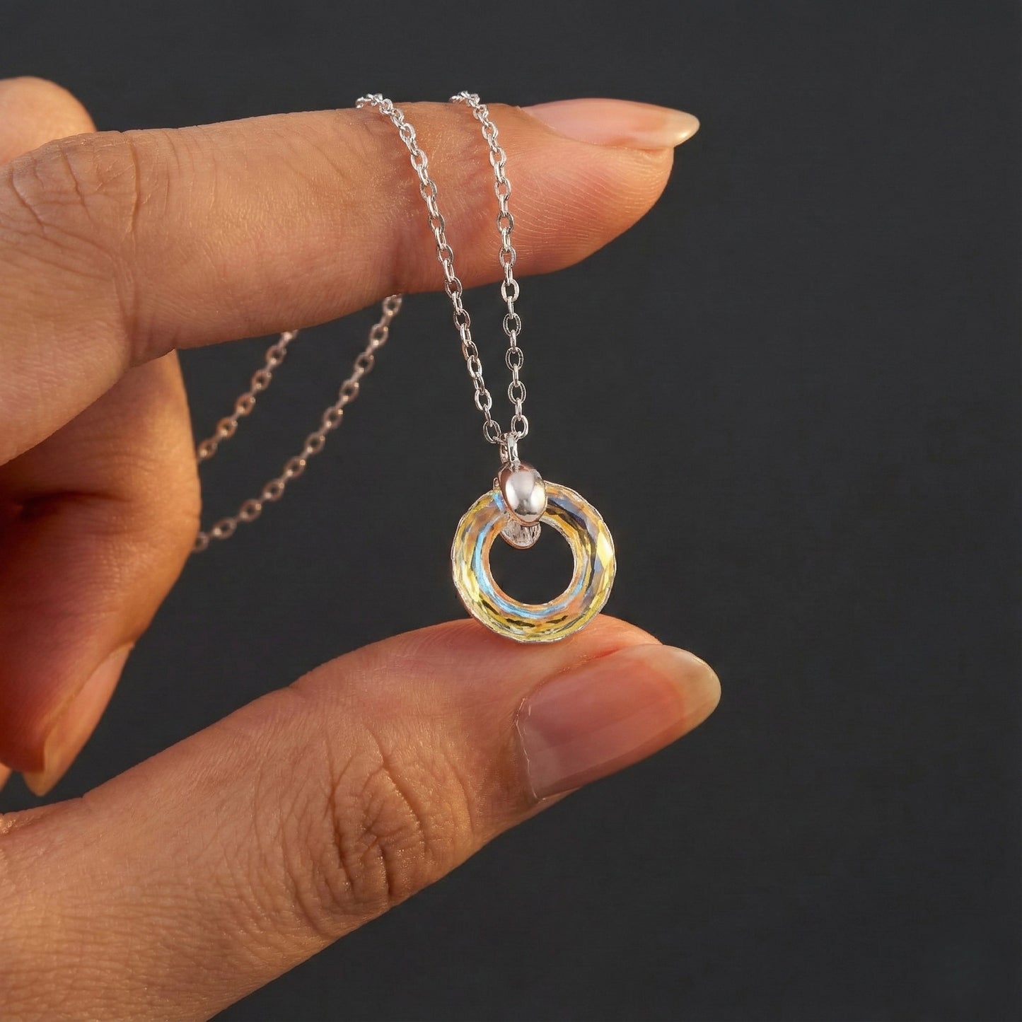 Hand holding a necklace with a pendant against a dark background