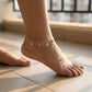 Anchored anklet on a foot with snowflake charms, standing on a tiled floor.