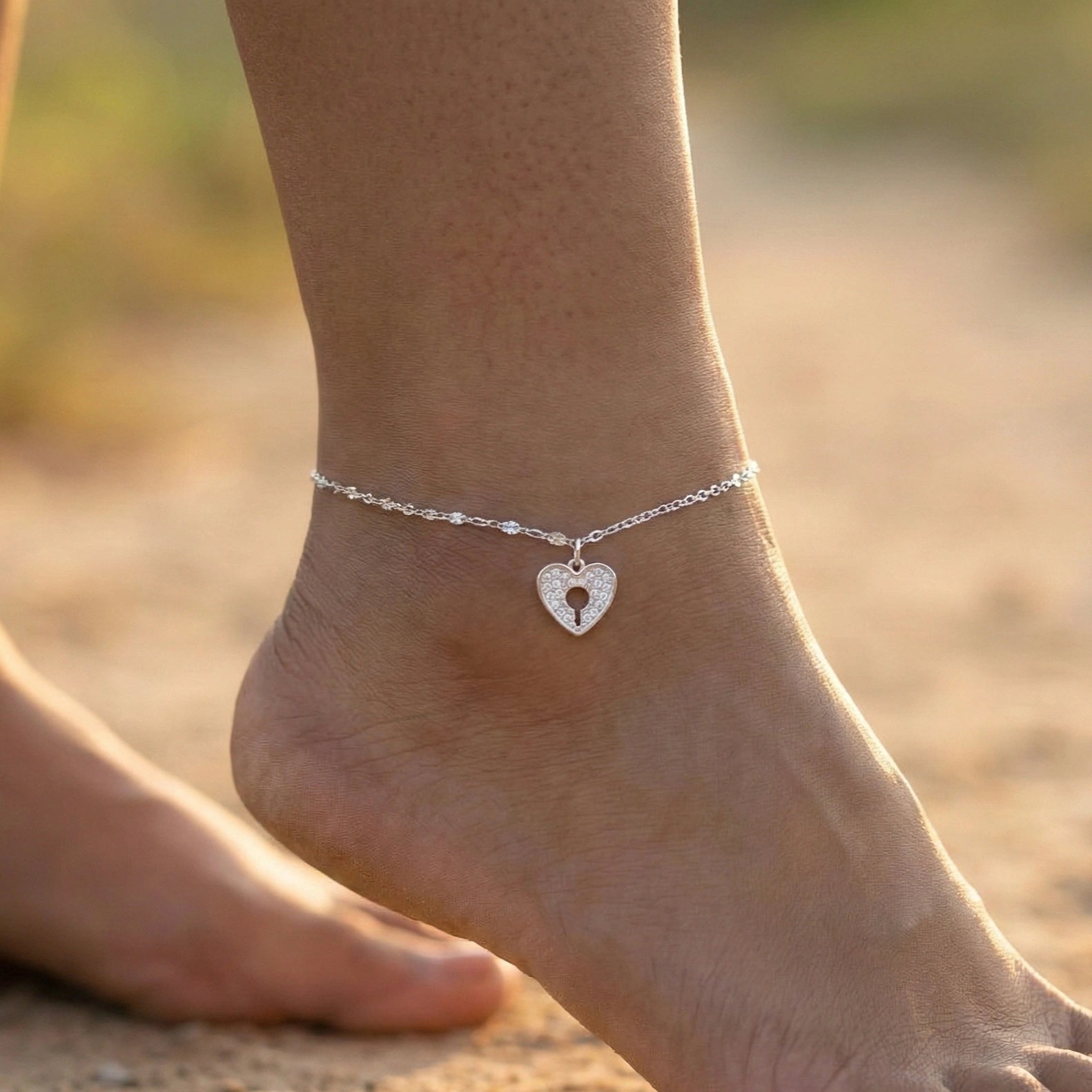Silver anklet with a heart-shaped charm on a foot against a blurred natural background