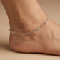 Triple-layered ankle bracelet on a foot against a beige background