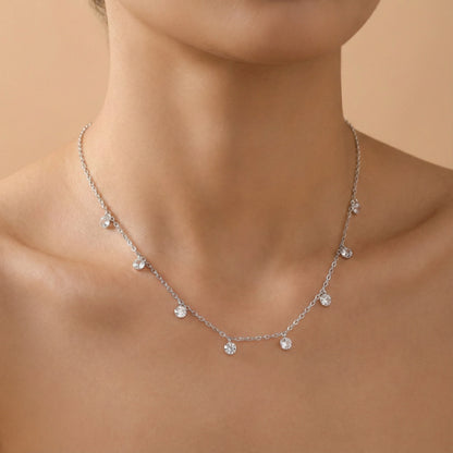 Silver necklace with small pendants on a person against a beige background