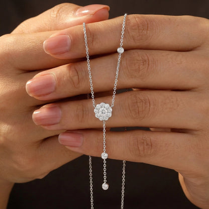 Silver necklace with a floral clasp held between fingers against a dark background