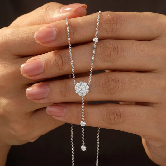 Silver necklace with a floral clasp held between fingers against a dark background