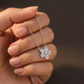 Silver necklace with a flower pendant held in a hand against a blurred background