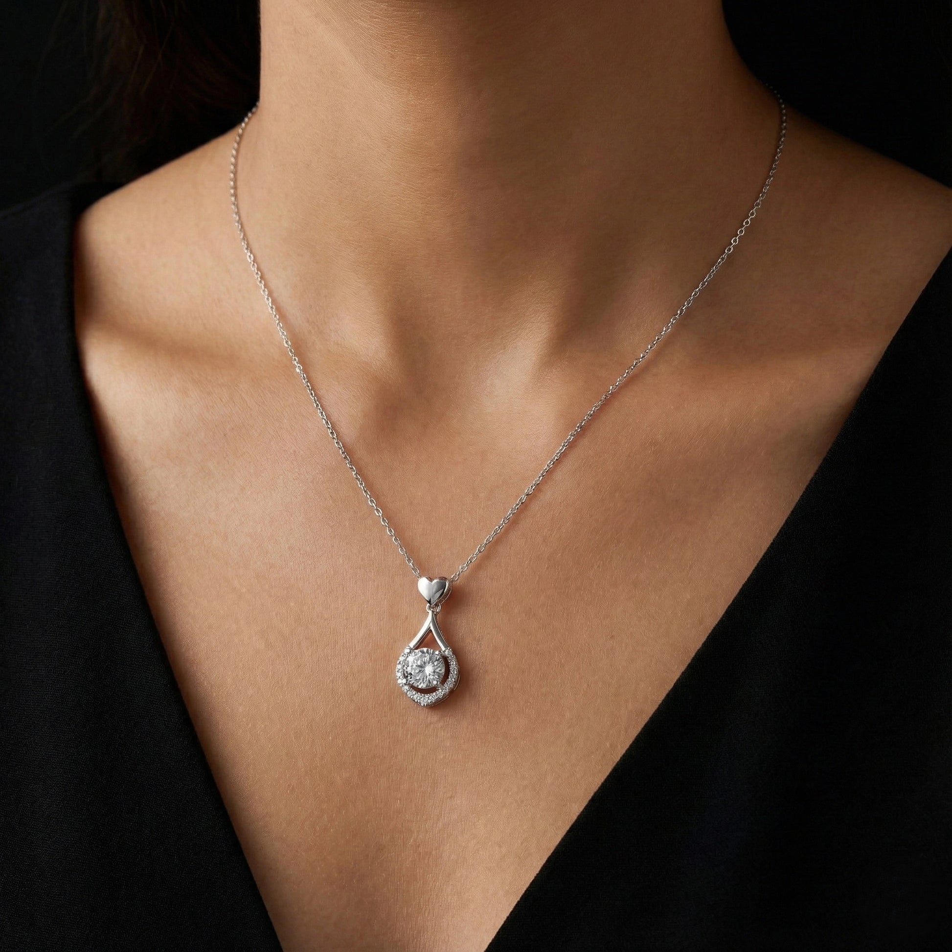 Silver necklace with a teardrop pendant on a person wearing a black top.