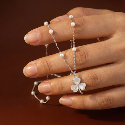 Silver necklace with a clover pendant held by a hand against a brown background