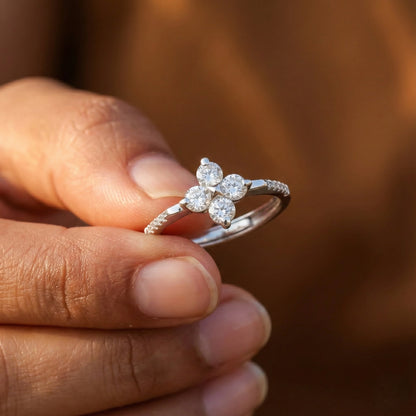 Silver floral ring held between fingers against a blurred brown background