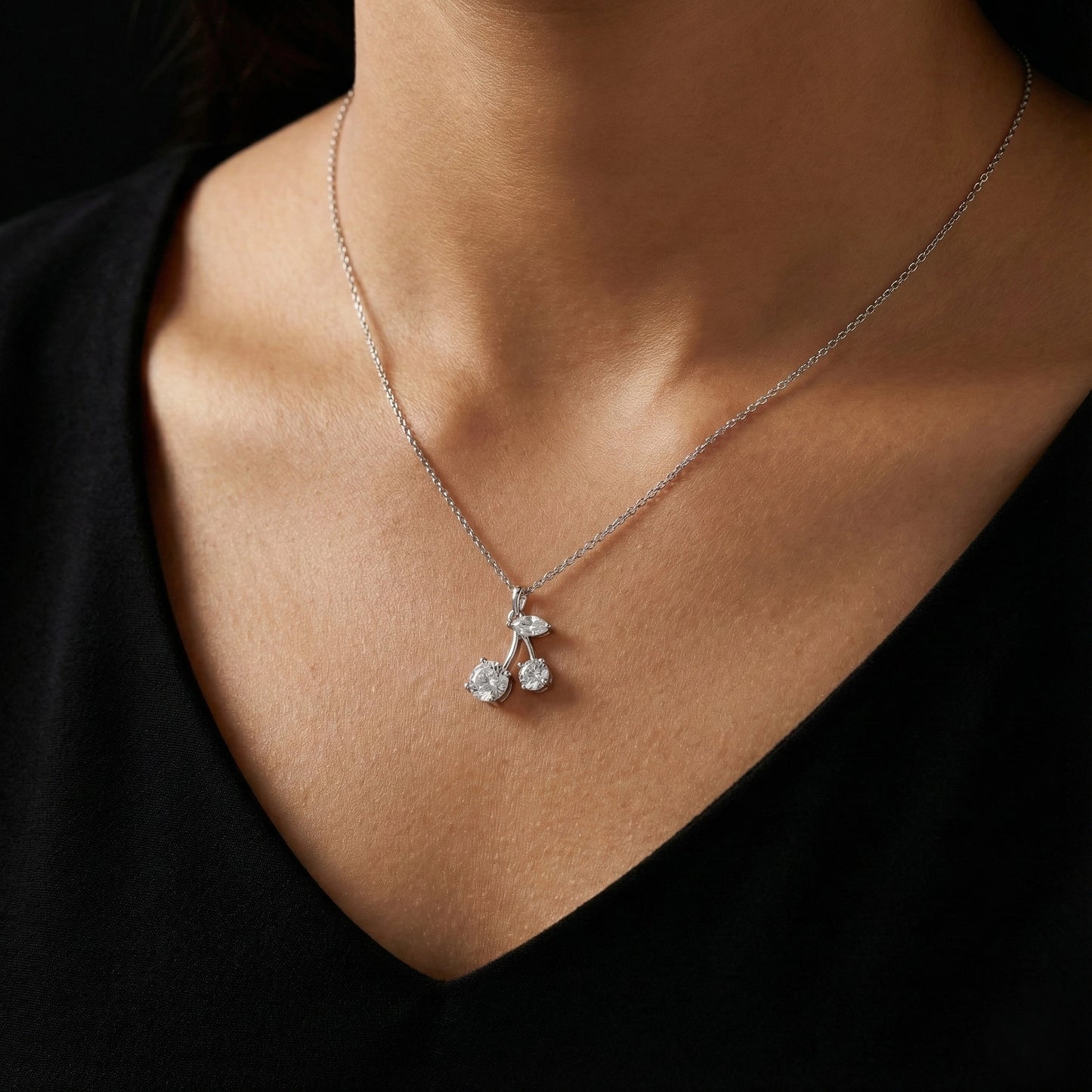 Silver necklace with a cherry pendant on a person wearing a black top.