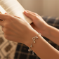 Close-up of a hand wearing a silver bracelet with charms, holding a book.