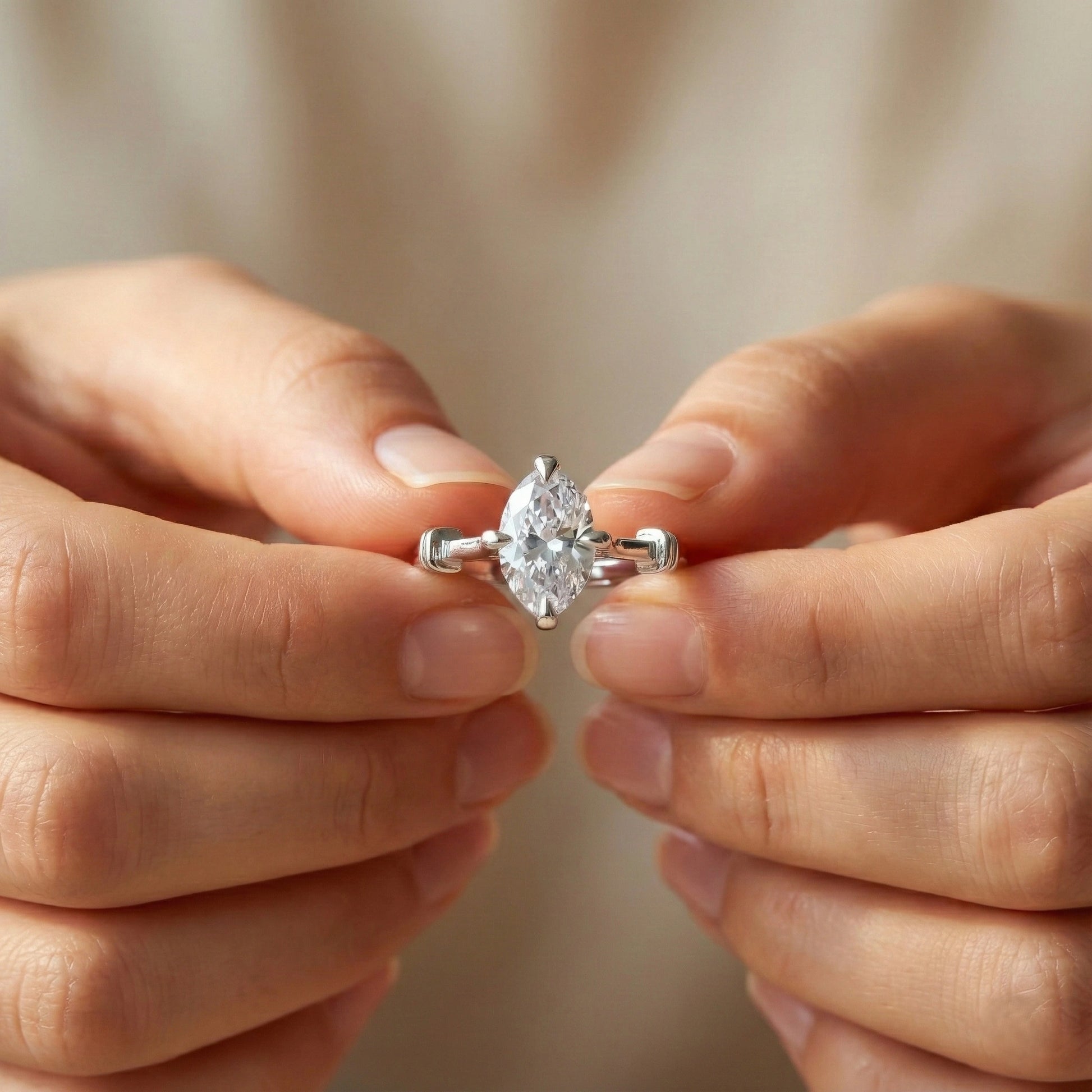 Diamond ring held between two hands against a neutral background