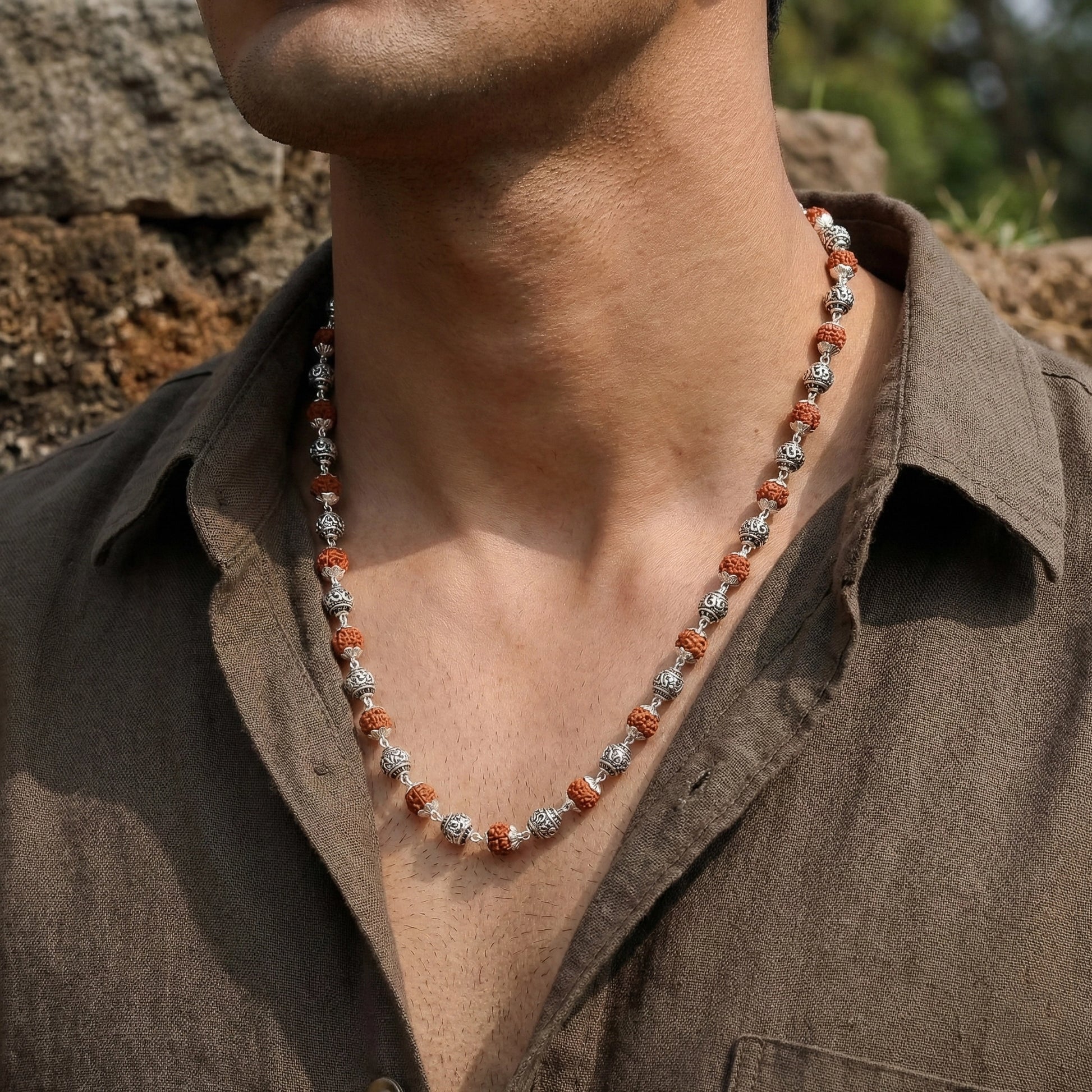 Necklace with red and silver beads worn by a person in a brown shirt outdoors.
