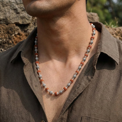 Necklace with red and silver beads worn by a person in a brown shirt outdoors.
