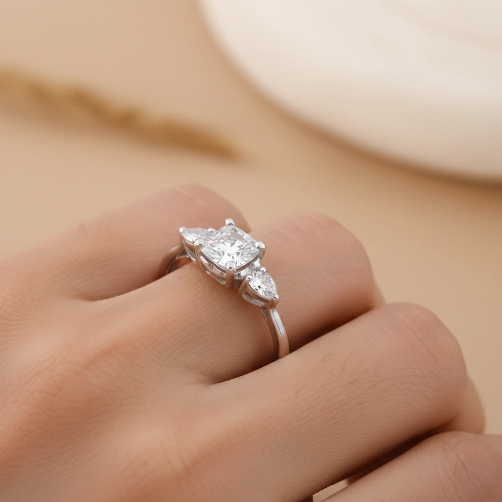 Silver ring with pear-shaped diamonds on a hand against a beige background