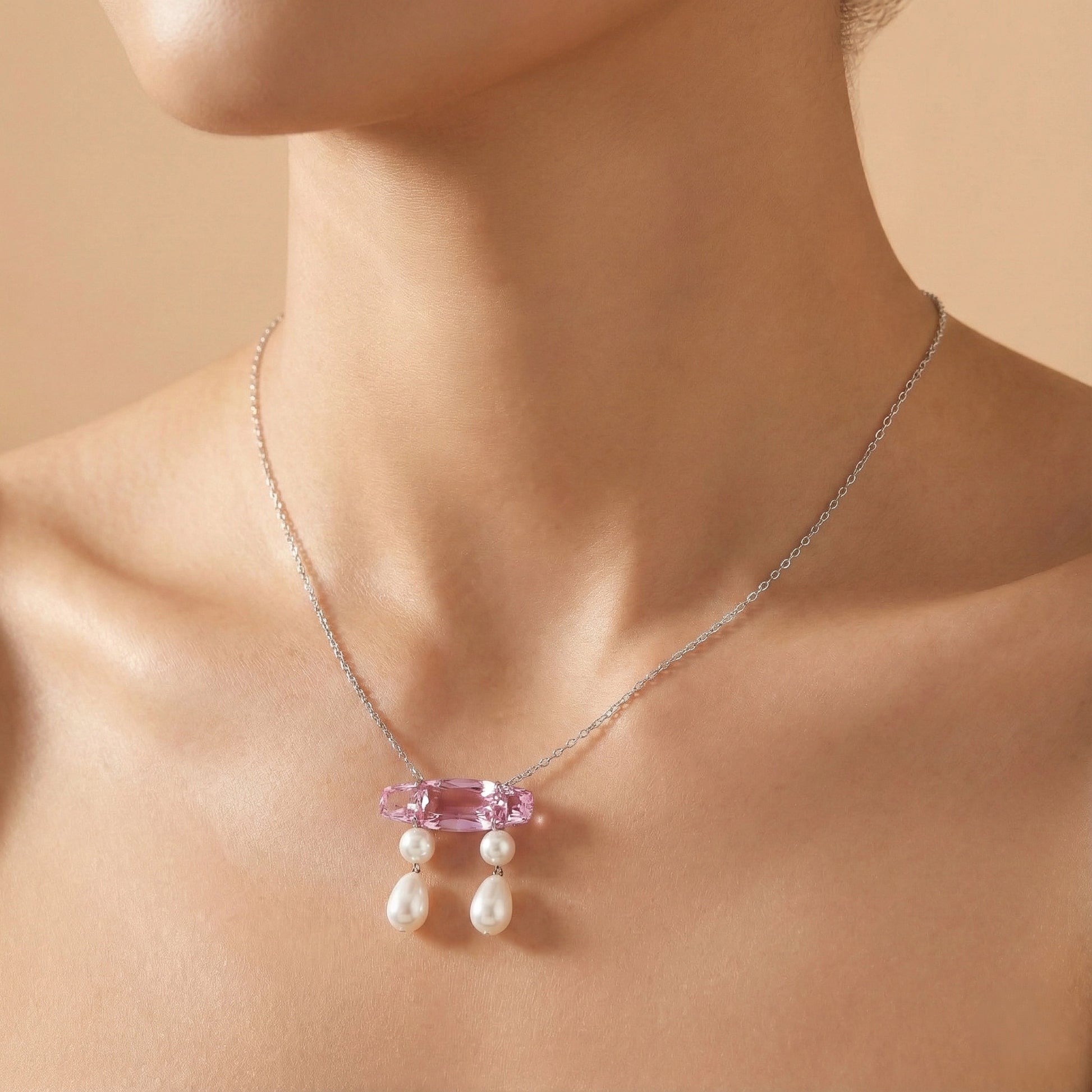 Necklace with pink gemstone and pearls on a model against a beige background