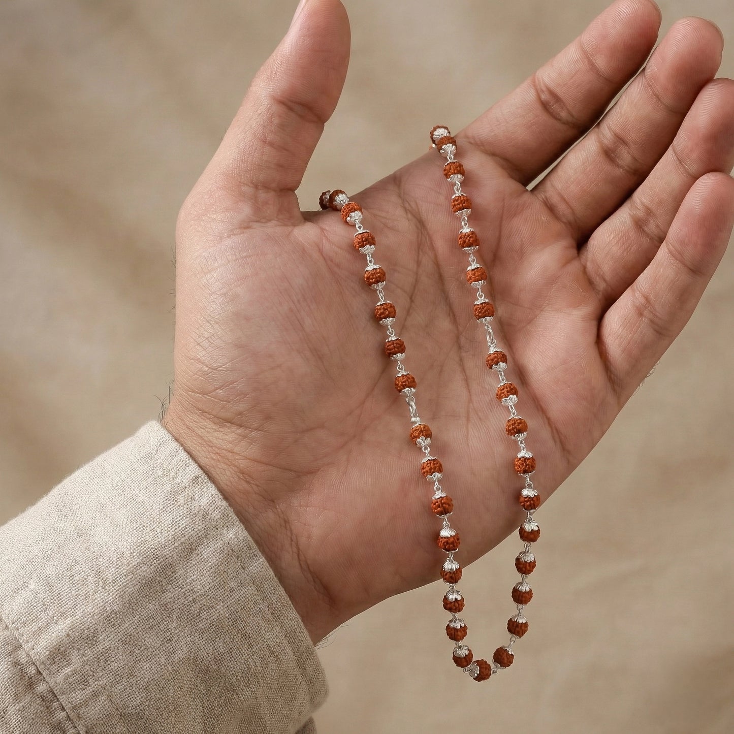 Hand holding a string of brown and white beads against a neutral background