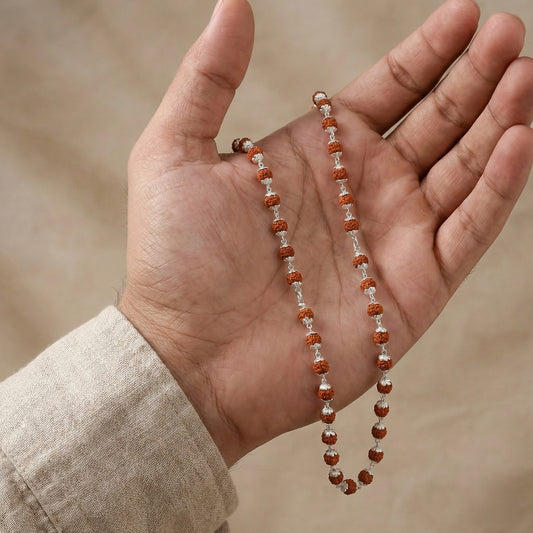 Hand holding a string of brown and white beads against a neutral background