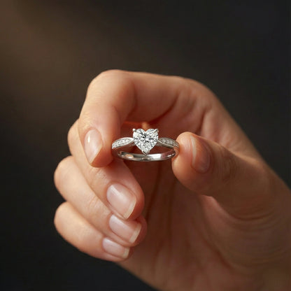 Heart-shaped diamond ring held in a hand against a dark background