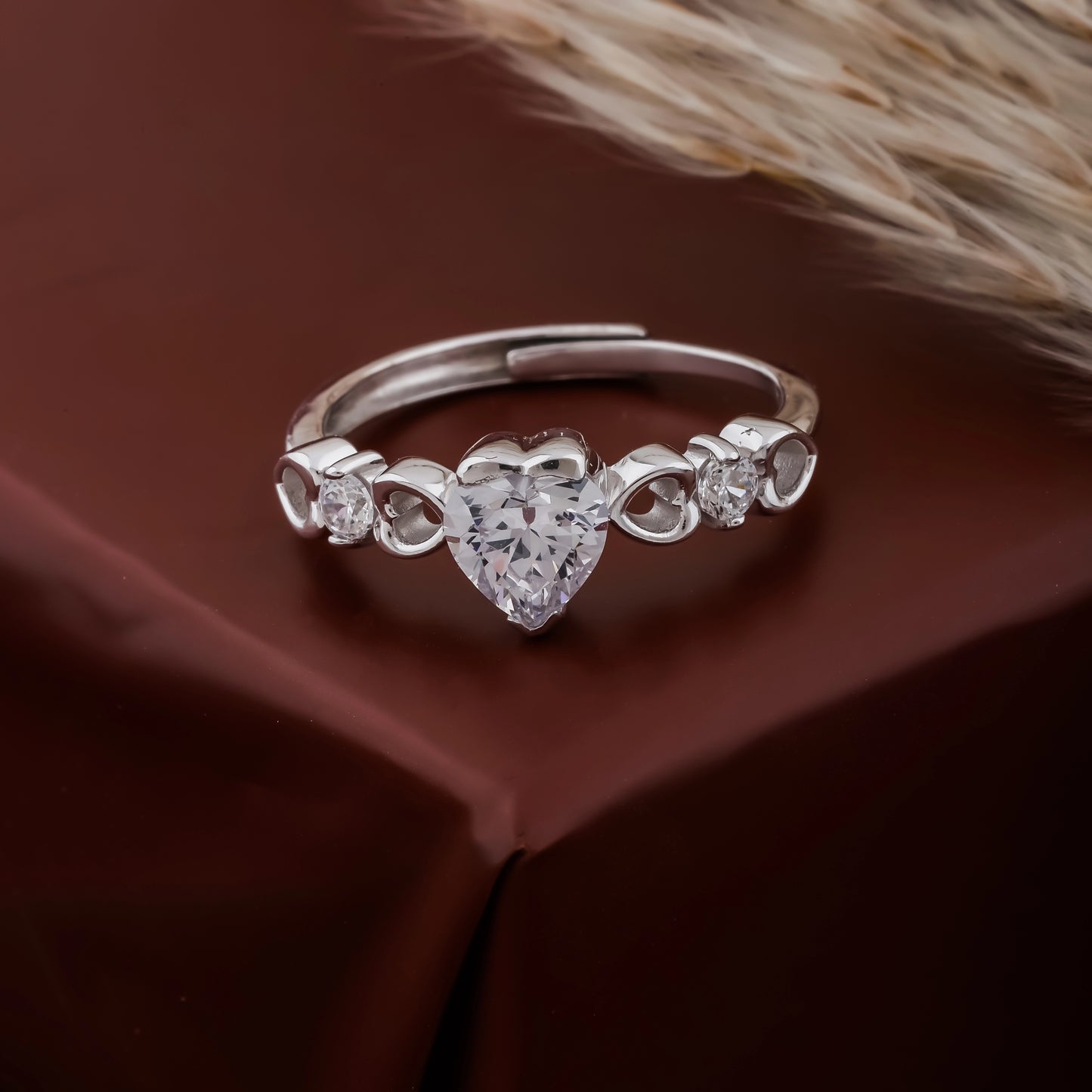 Silver ring with heart-shaped diamond on a brown fabric background