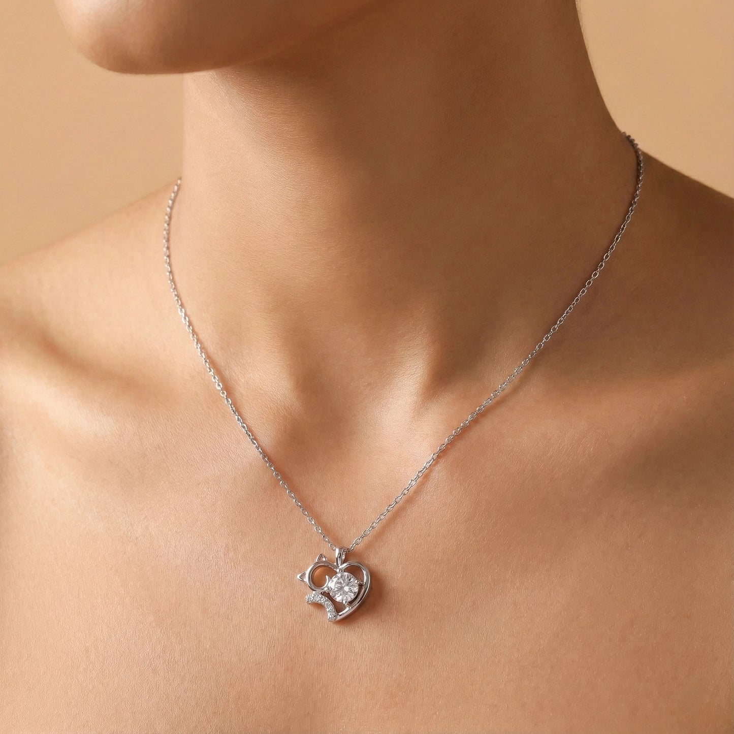 Silver necklace with a heart-shaped pendant on a person against a beige background