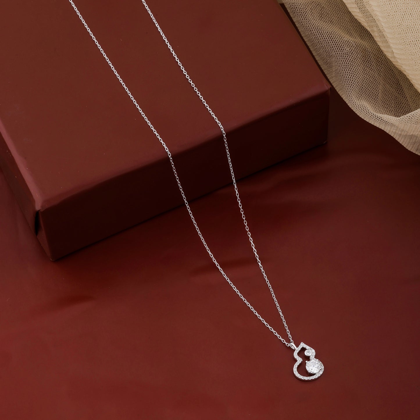 Silver necklace with a heart-shaped pendant on a red surface