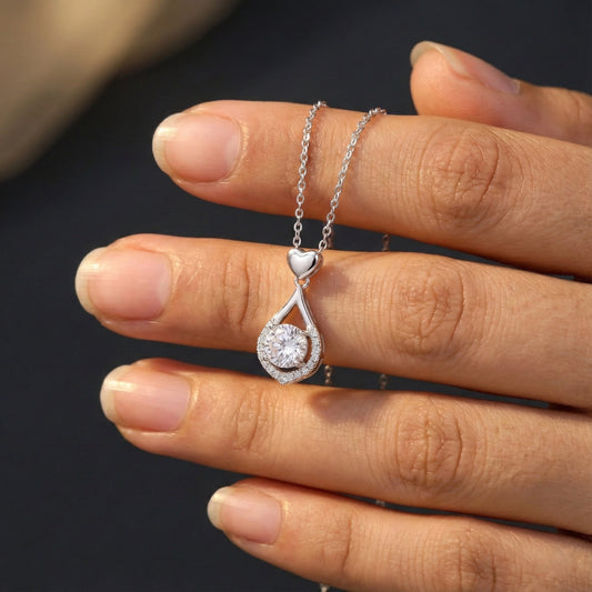 Silver necklace with a heart-shaped pendant on a hand against a dark background