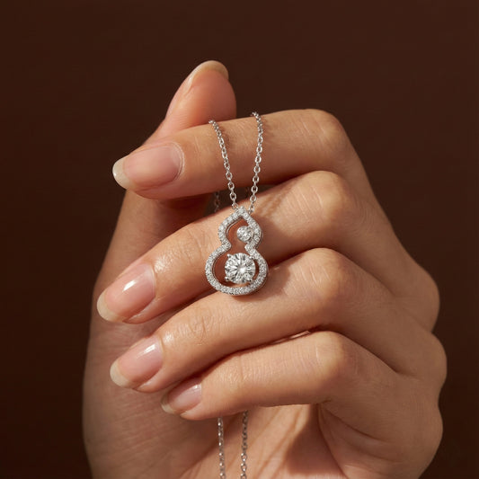 Hand holding a silver necklace with a diamond pendant against a brown background