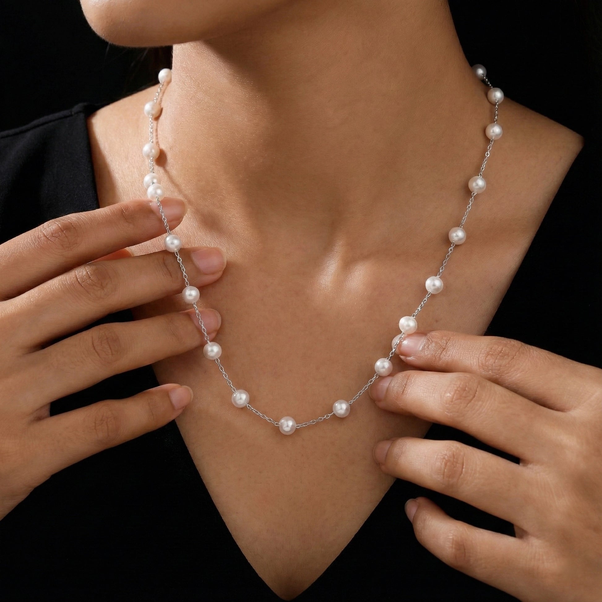 Pearl necklace being worn and adjusted by a person against a black background