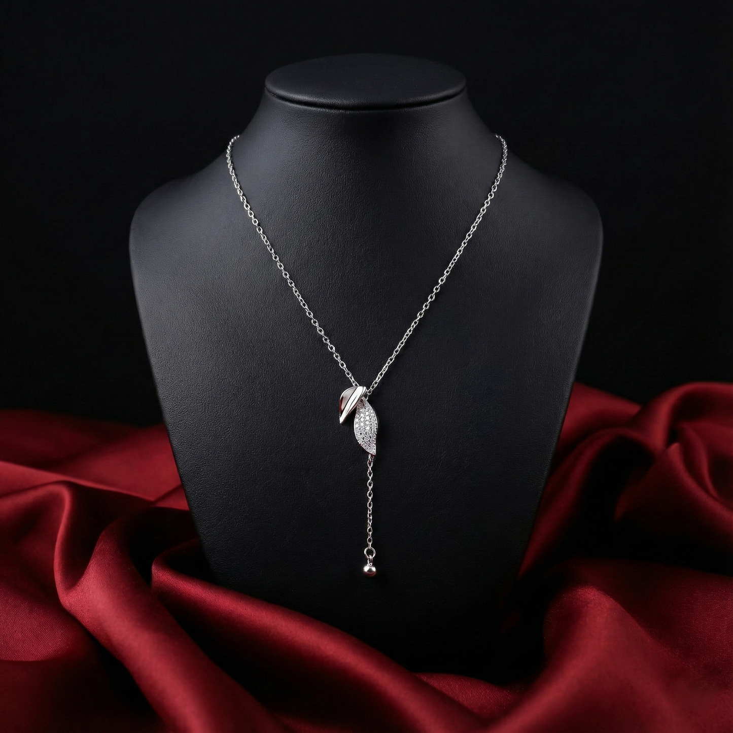 Silver necklace with leaf pendant on a black mannequin bust against a dark background