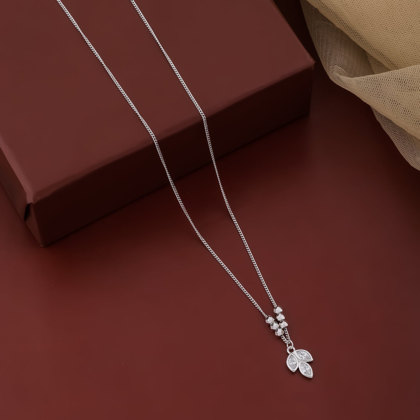 Silver necklace with a leaf pendant on a brown surface