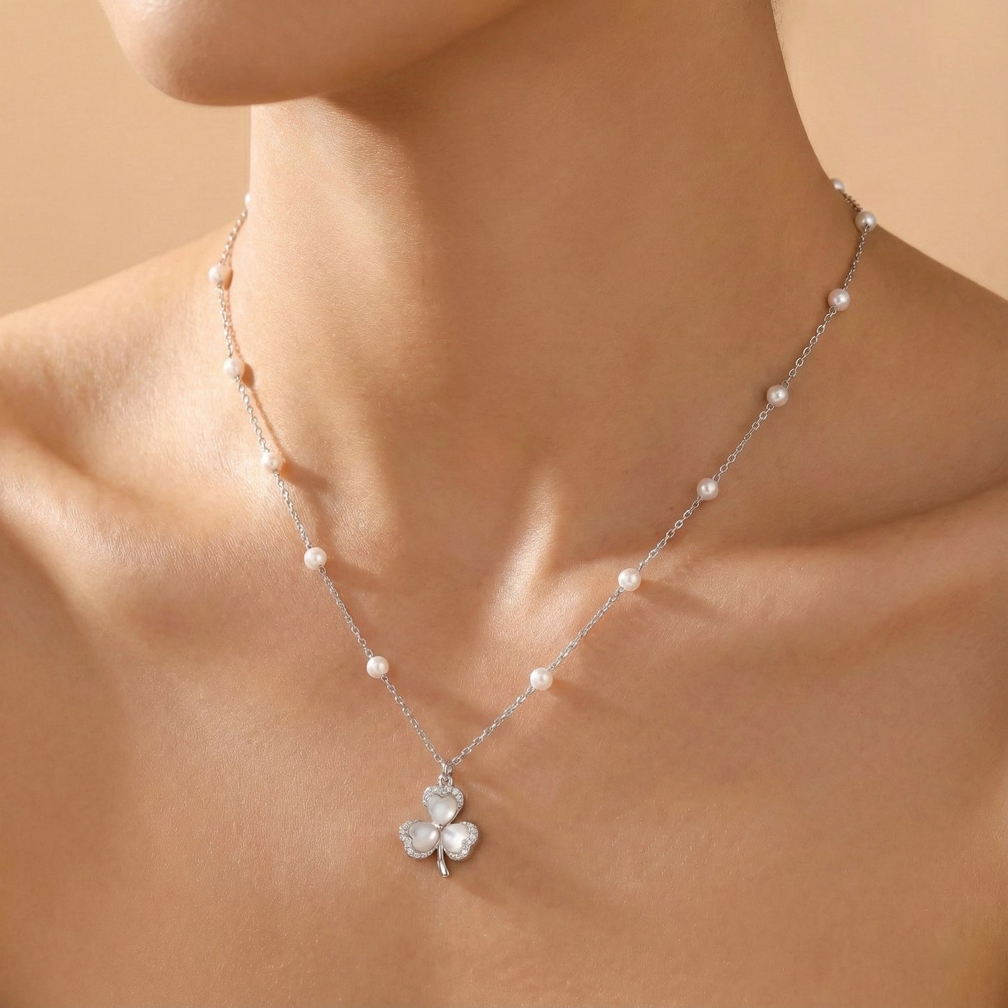Pearl necklace with a clover pendant on a person against a beige background