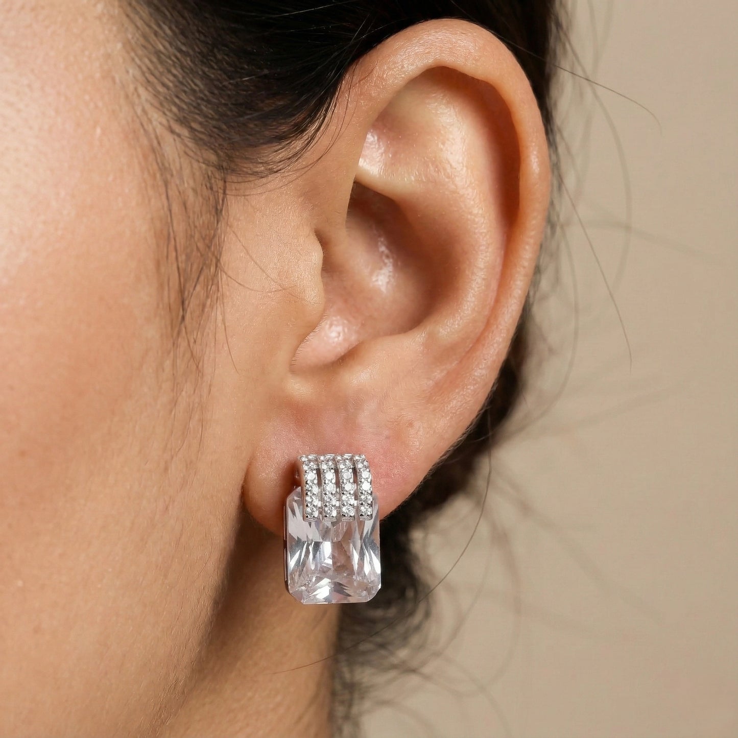 Close-up of an ear wearing a diamond earring with a neutral background