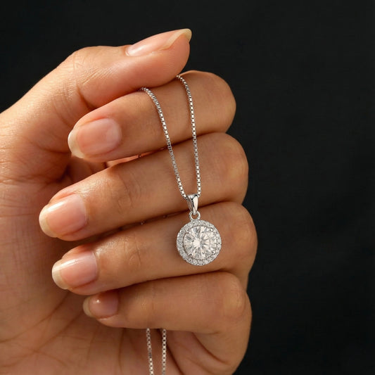Silver necklace with a round pendant held in a hand against a black background