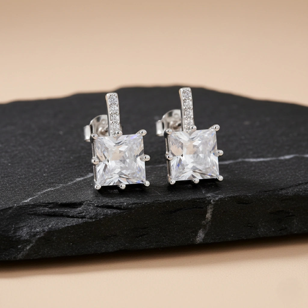 Pair of silver square-cut gemstone earrings on a dark stone surface.