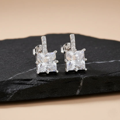 Pair of silver square-cut gemstone earrings on a dark stone surface.
