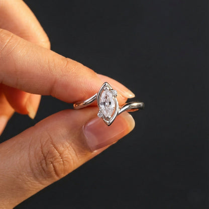 Silver ring with a diamond held between fingers against a dark background