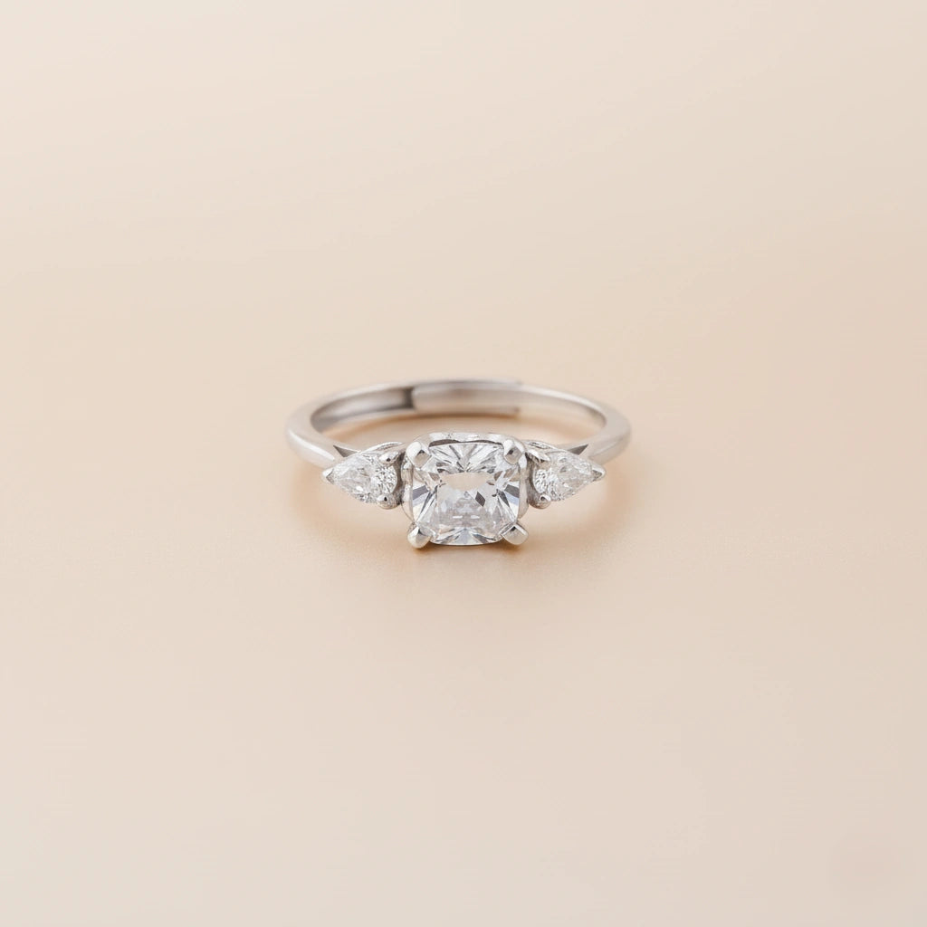 Silver ring with a central diamond and two smaller diamonds on a beige background