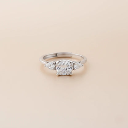Silver ring with a central diamond and two smaller diamonds on a beige background