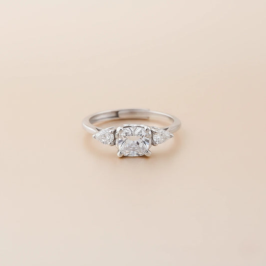Silver ring with a central diamond and two smaller diamonds on a beige background