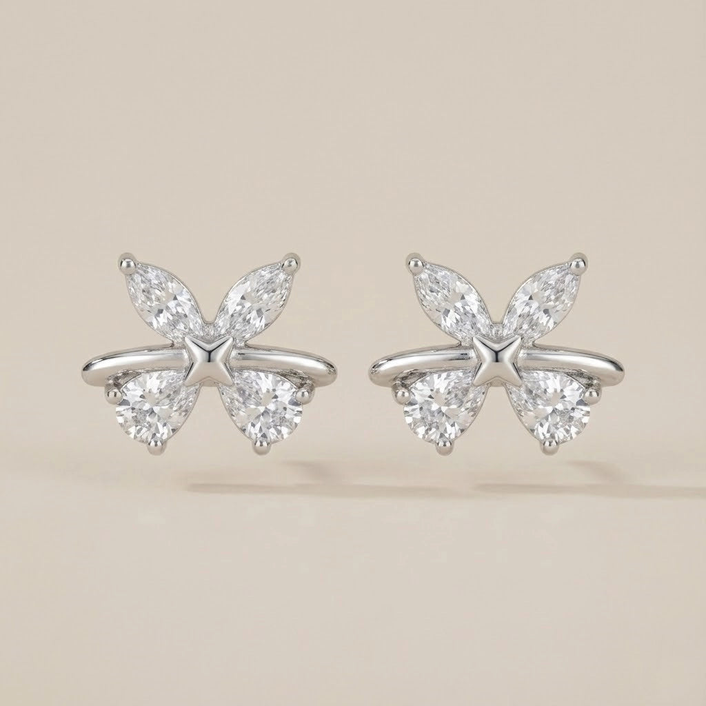 Butterfly-shaped silver earrings with clear gemstones on a beige background