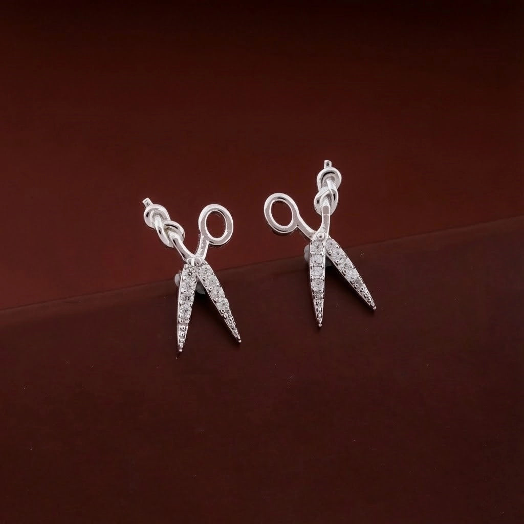 Silver scissors-shaped earrings on a dark brown background