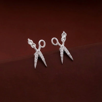 Silver scissors-shaped earrings on a dark brown background
