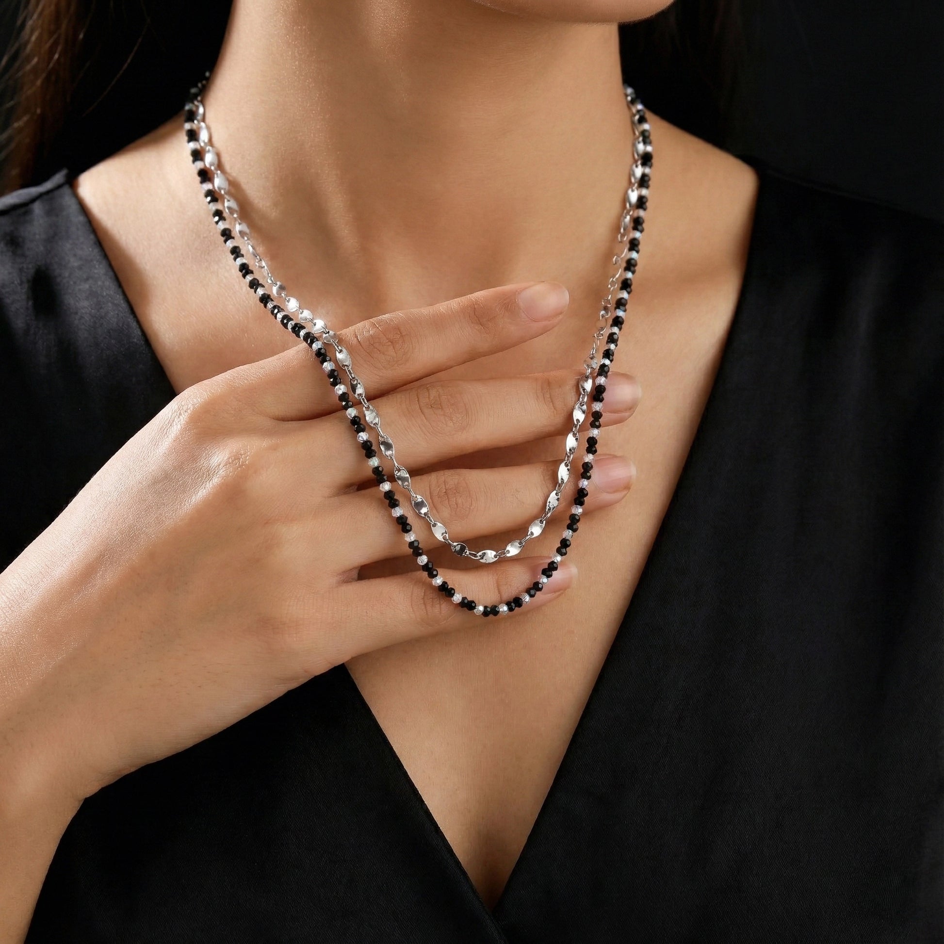 Person wearing a black and silver beaded necklace, holding it with their hand.