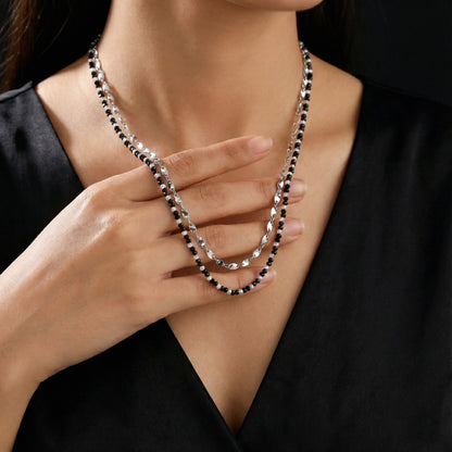 Person wearing a black and silver beaded necklace, holding it with their hand.