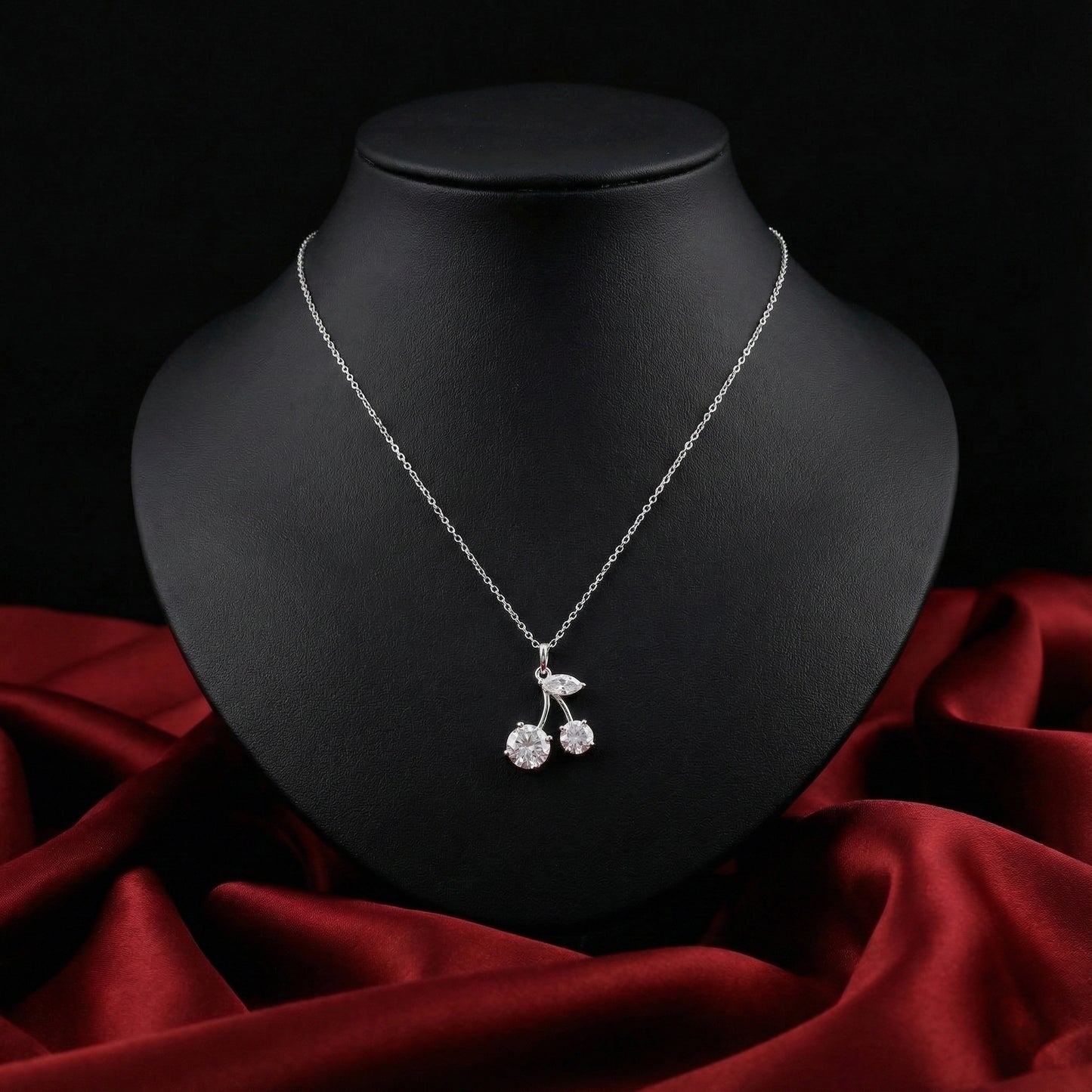 Silver necklace with a cherry pendant on a black mannequin bust against a red fabric background