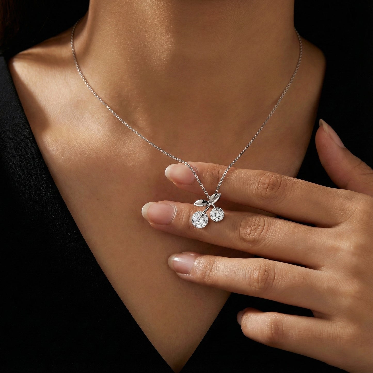 Silver necklace with a cherry pendant worn by a person against a dark background