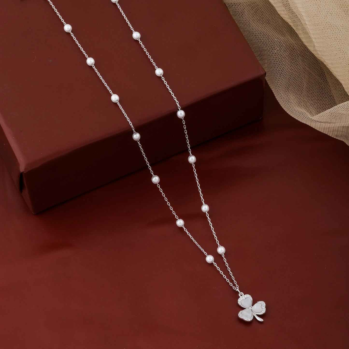 Silver necklace with a clover pendant on a red fabric background