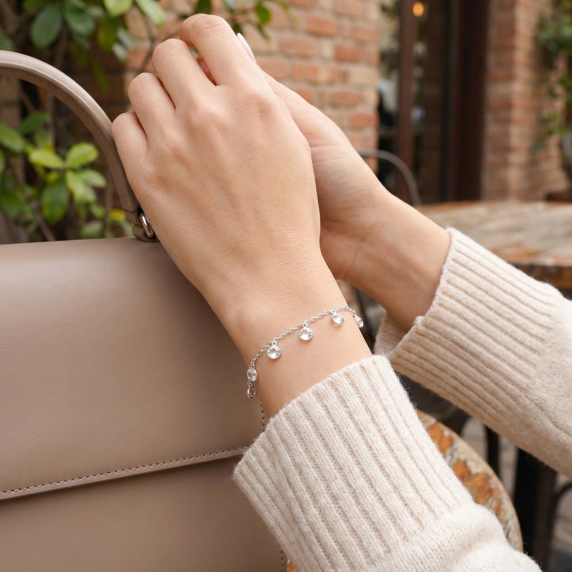 Close-up of a hand wearing a silver bracelet with a blurred outdoor background